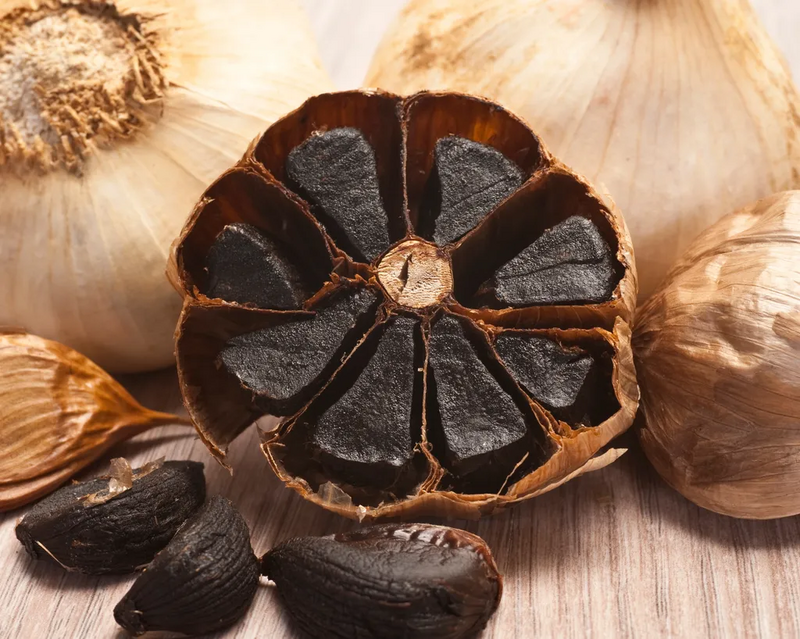 Nahaufnahme von schwarzem Knoblauch – gereifte Knoblauchknollen mit dunklen, weichen Zehen, umgeben von der hellbraunen Schale.