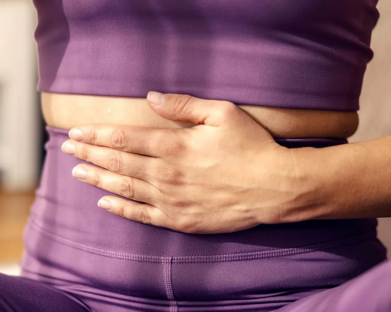 Person in lila Sportkleidung legt die Hände auf den Unterbauch.