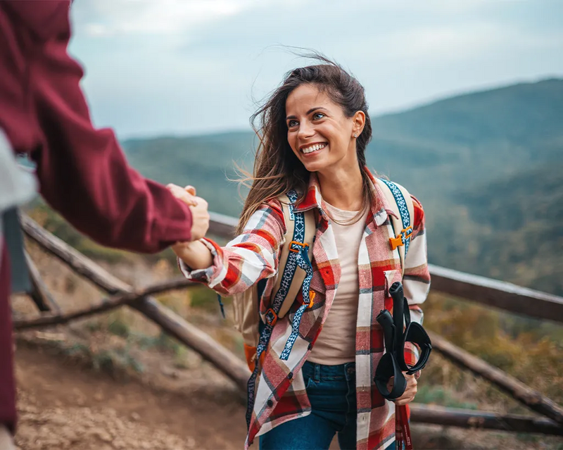 Junge Frau nimmt beim Wandern eine Hand zur Unterstützung entgegen