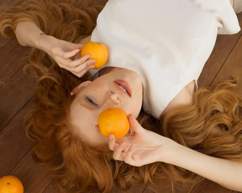 Bild von einer liegenden Frau, die Orangen als Quelle von Vitamin C in ihren Händen hält