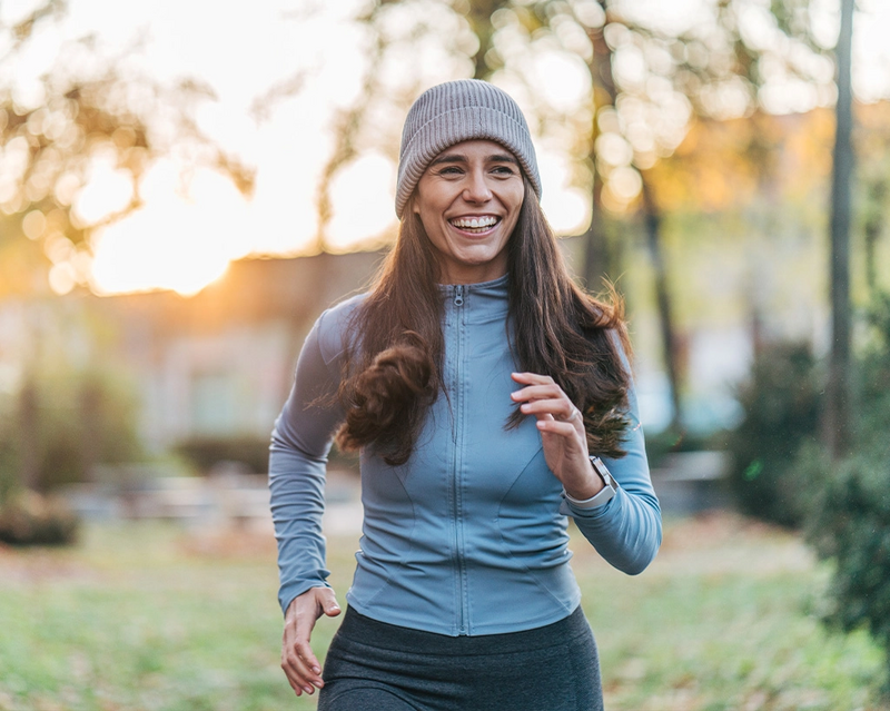 Eine lächelnde Frau beim Joggen in einem Park bei Sonnenuntergang